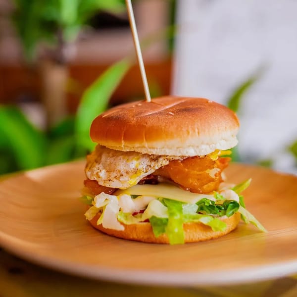 A fish burger with a fried egg, cheese, and lettuce on a wooden plate.