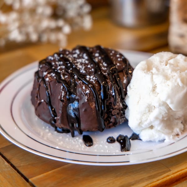 Chocolate lava cake drizzled with chocolate sauce and powdered sugar, served with vanilla ice cream.
