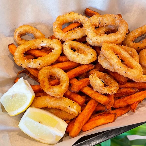 Golden fried calamari rings and sweet potato fries with two lemon wedges in a basket.