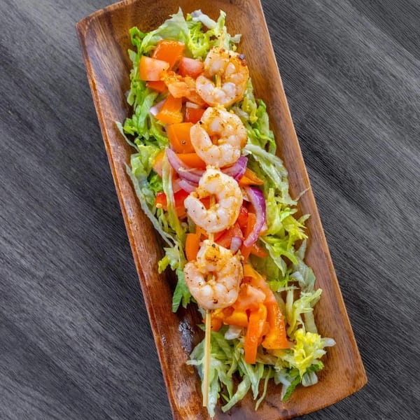 Grilled shrimp skewer with lettuce, tomatoes, and red onions on a wooden platter.
