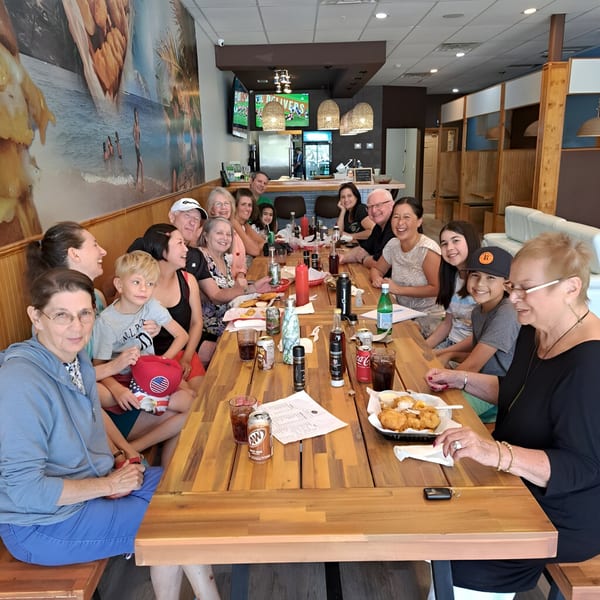 A large group of people of all ages enjoying fish and chips at a long wooden table.