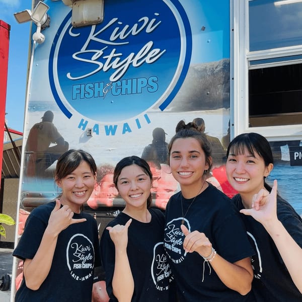 Four smiling women in black Kiwi Style Fish and Chips shirts pose in front of their food truck.