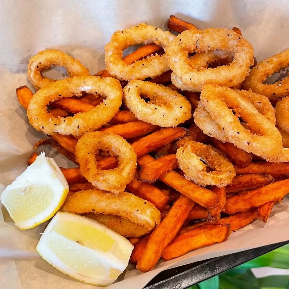 Crispy fried calamari rings and sweet potato fries served with two lemon wedges.