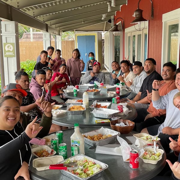 A large group of people enjoying Kiwi Style Fish and Chips meals at outdoor tables.